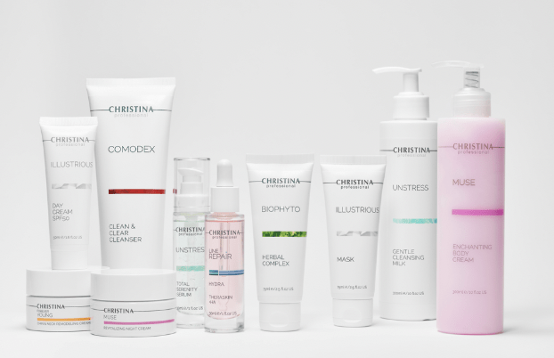 Assorted Christina skincare products lined up on a white surface, including cleansers, serums, masks, and creams (professional line).